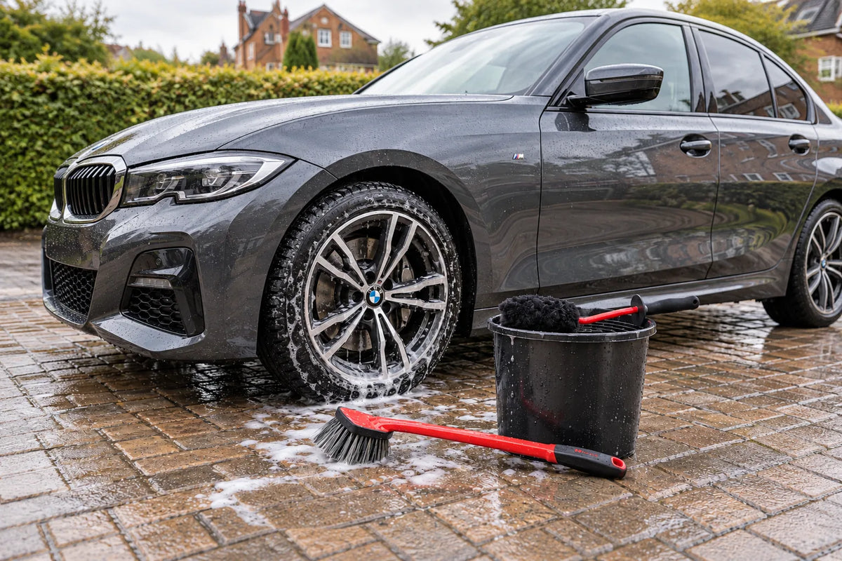 Maxshine Ultimate Wool Wheel Brush on a wash bucket and Soft Grip Tyre and Wheel Brush beside a grey BMW 3 Series on a wet driveway