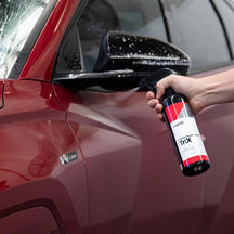 CarPro TRIX Iron And Tar Remover sprayed by hand onto a red car beside the mirror
