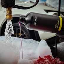 Autobead Pure Shampoo 2300:1 pink shampoo poured from the bottle into suds beside a running hose