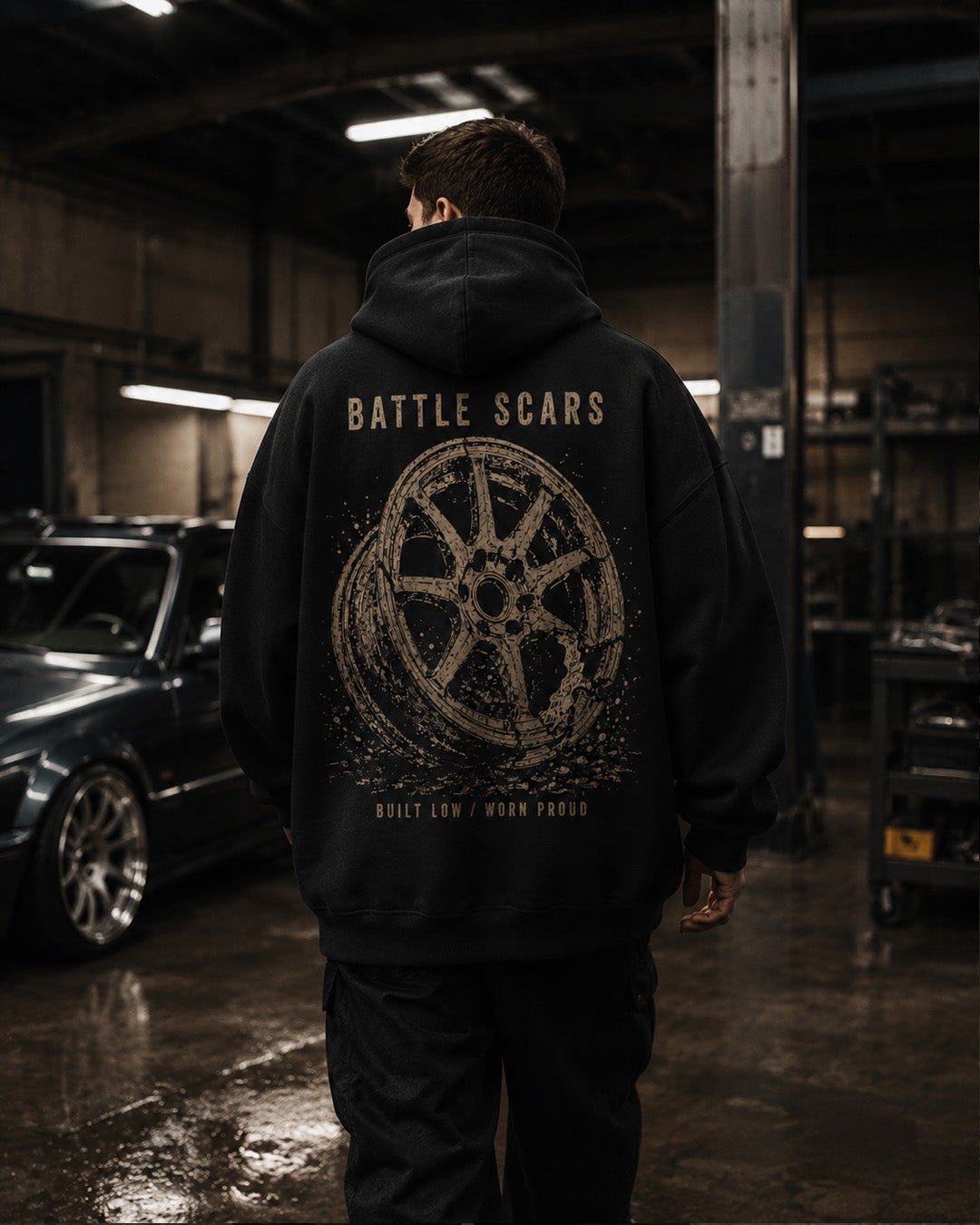 EuroStance Battle Scars Hoodie worn by a model in a garage, distressed wheel back print
