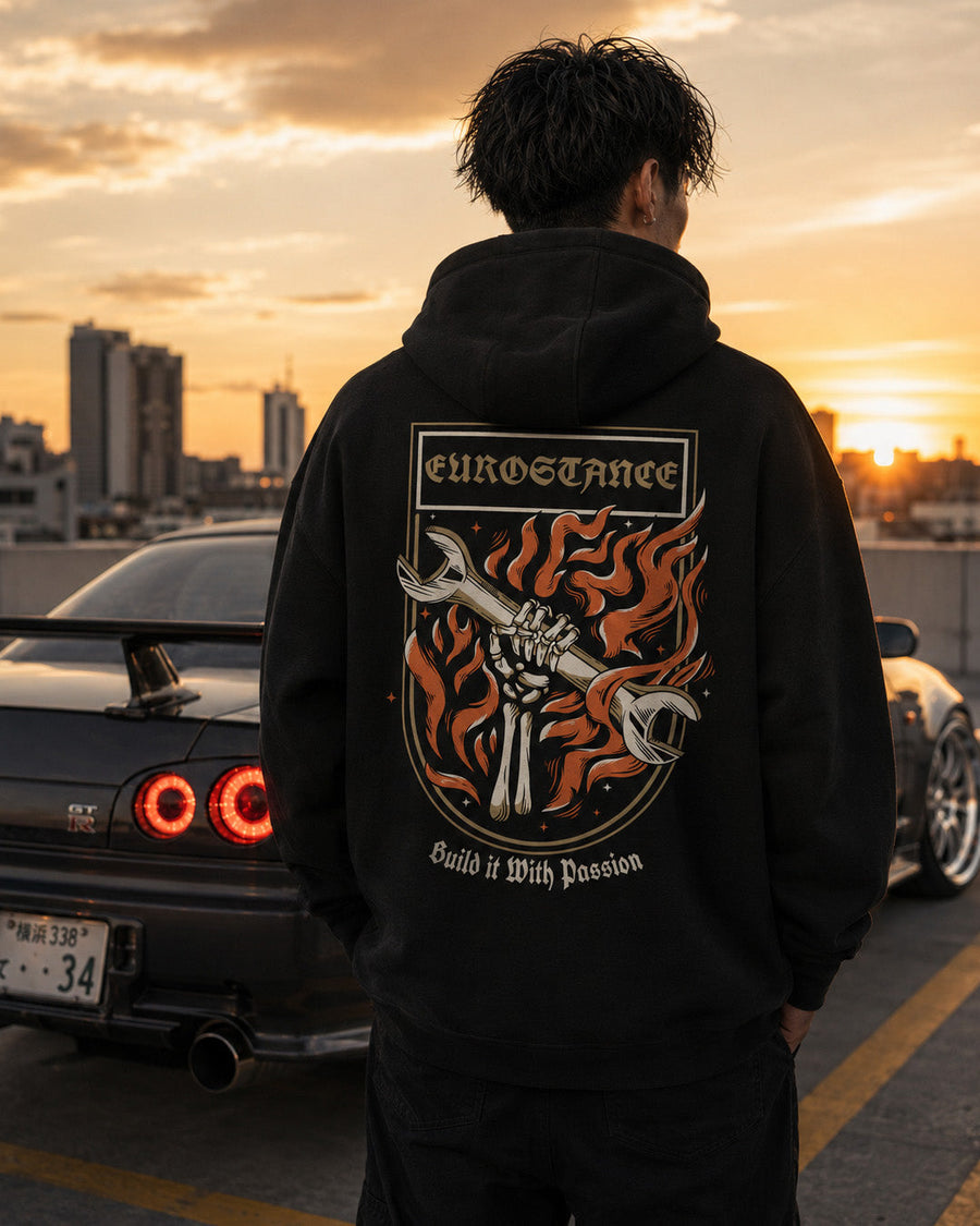 EuroStance Build it with Passion Hoodie worn at sunset, back flaming spanner print beside a car