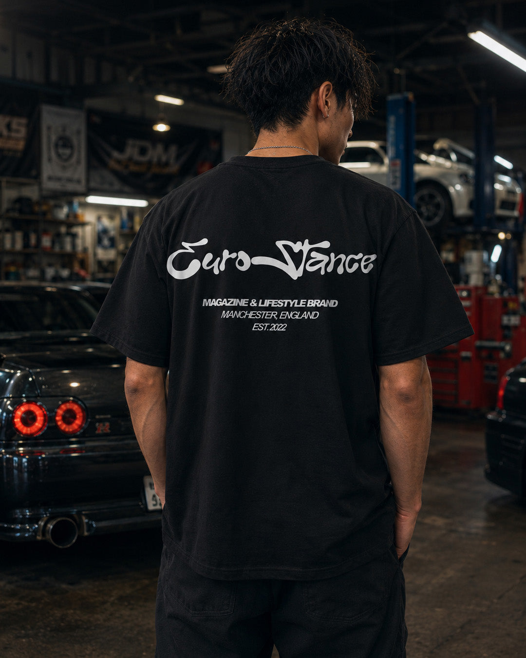 EuroStance Lifestyle Script Tee in black, white script back print on a model in a garage