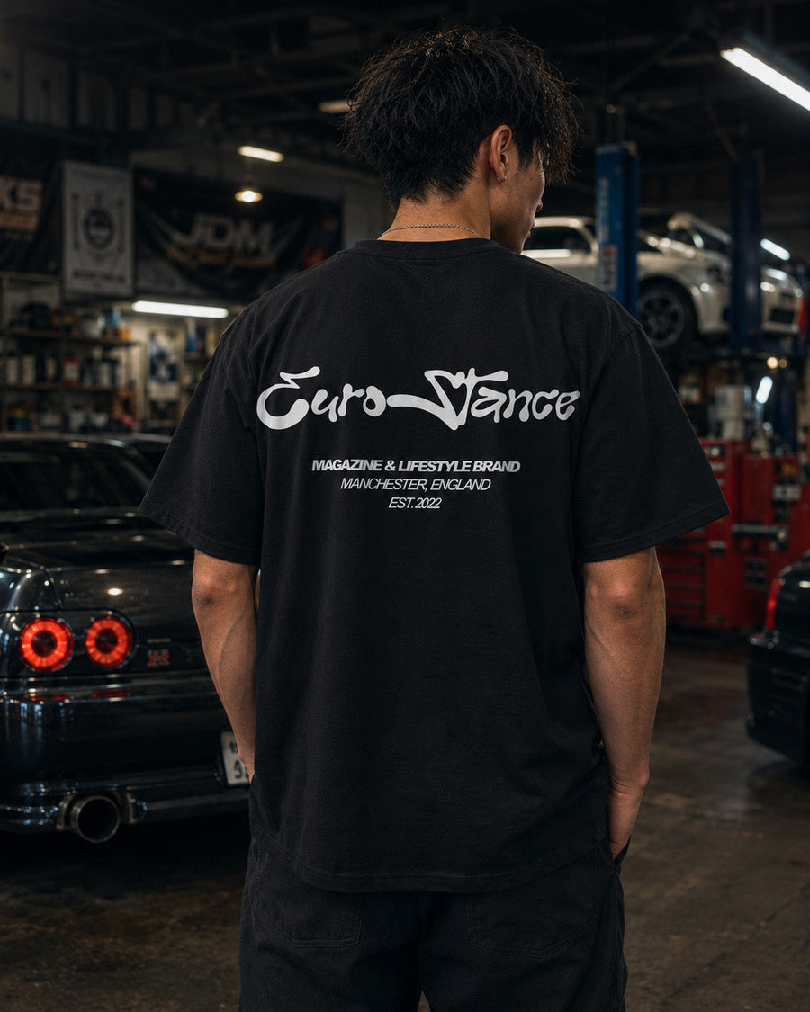 EuroStance Lifestyle Script Tee in black, white script back print on a model in a garage