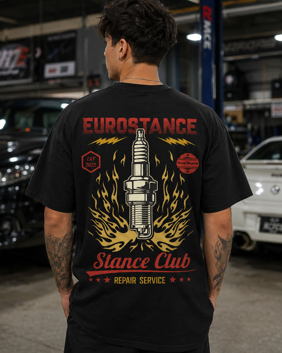 EuroStance SparkPlug Garage Tee in black worn in a workshop, flaming spark plug back print