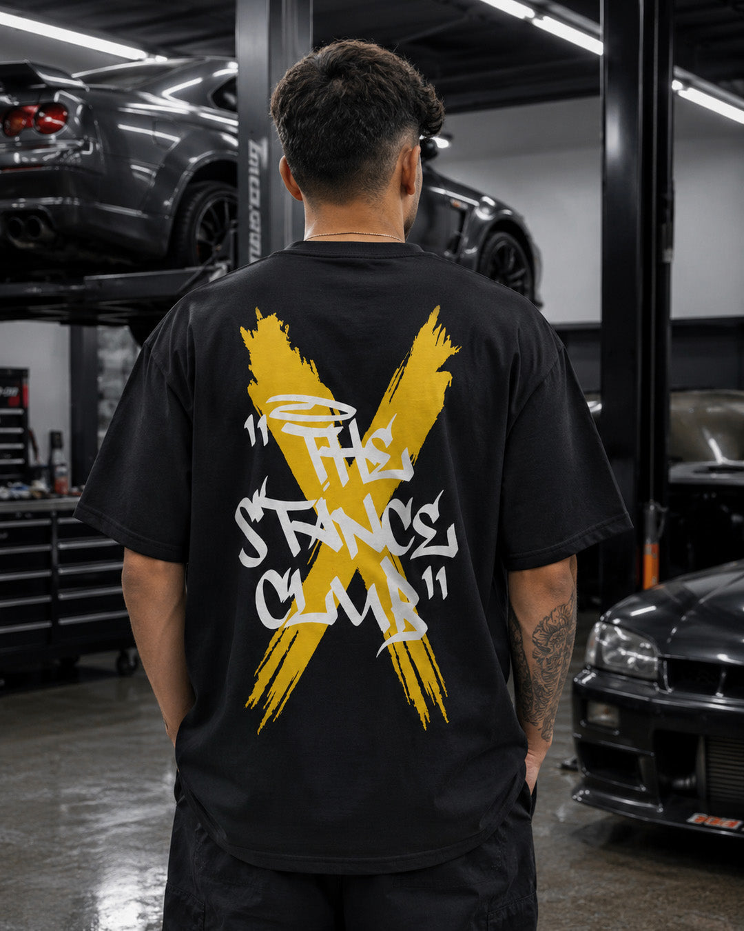EuroStance The Stance Club Tee worn from behind with yellow X back print in a garage