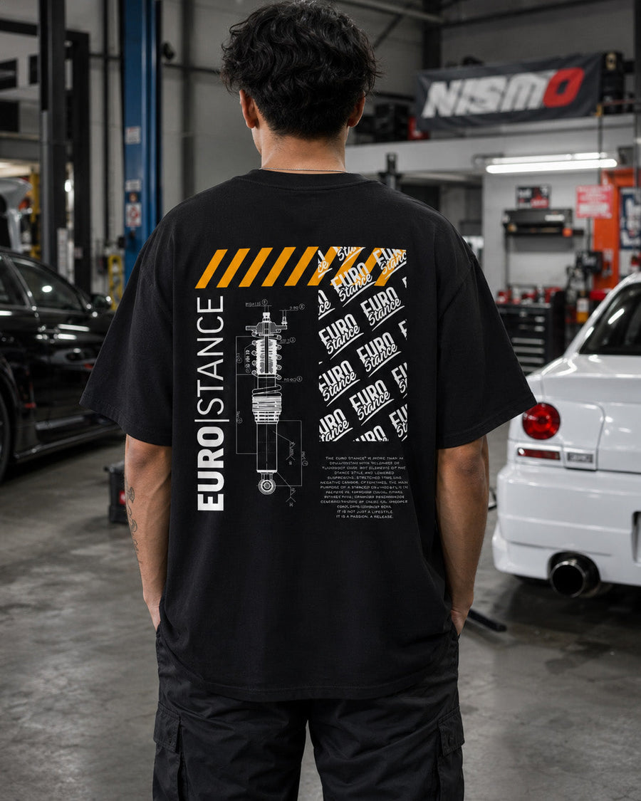 EuroStance Stance Defined T-Shirt, back print with coilover drawing worn by a man in a workshop