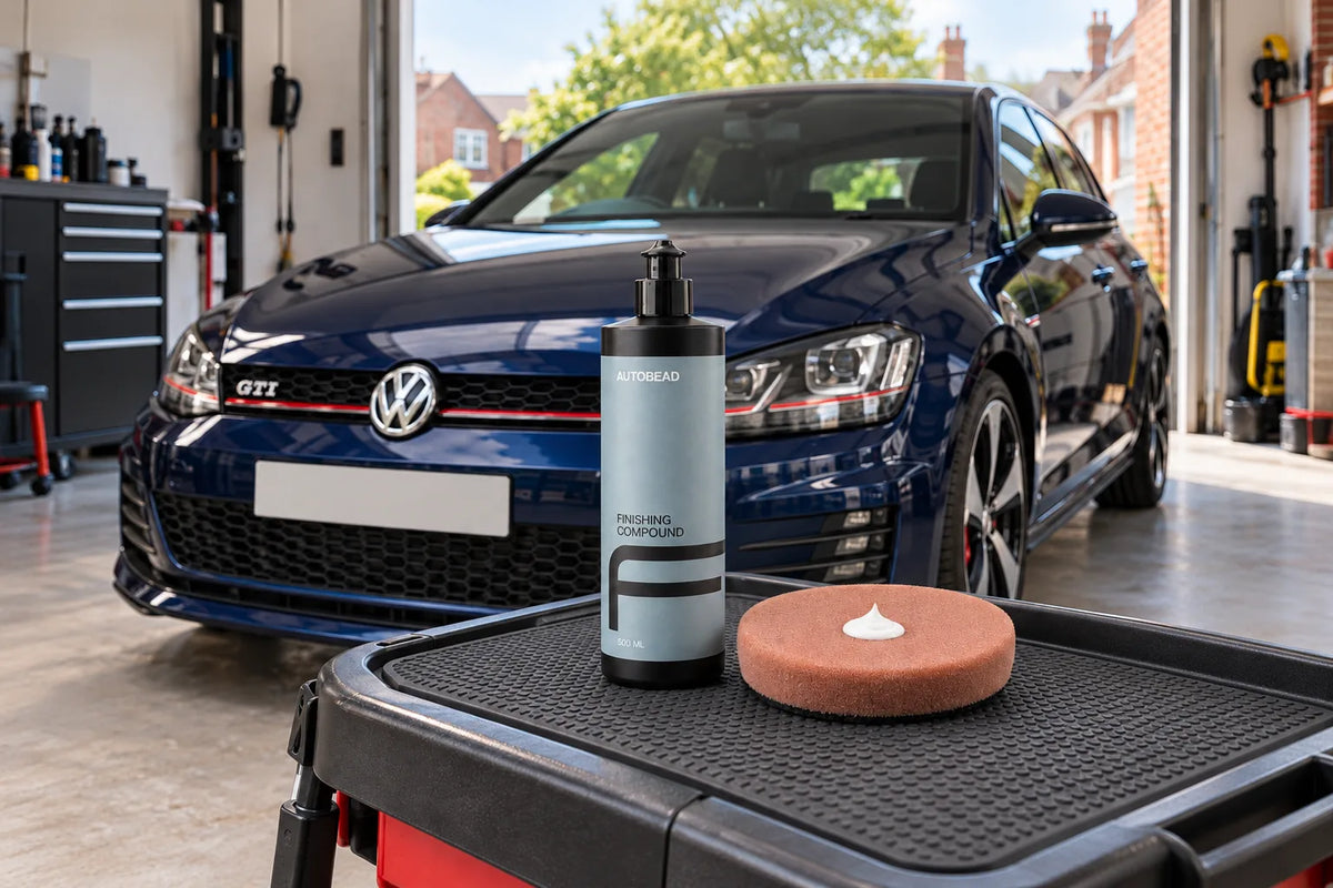 Autobead Finishing Compound and a Downforce Heavy Cut pad with a dab of compound on a detailing trolley in front of a dark blue Volkswagen Golf GTI Mk7 in a home garage