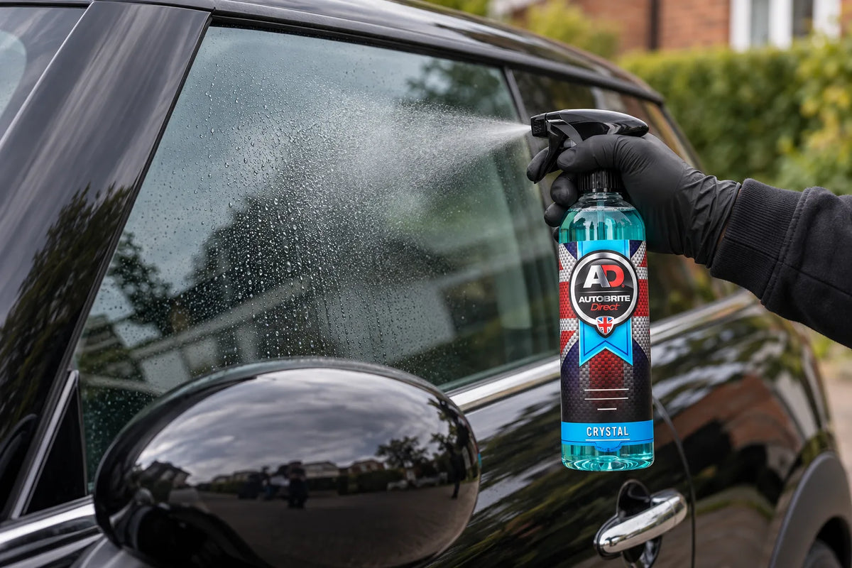 Autobrite Direct Crystal Glass Cleaner being sprayed onto the side window of a black car