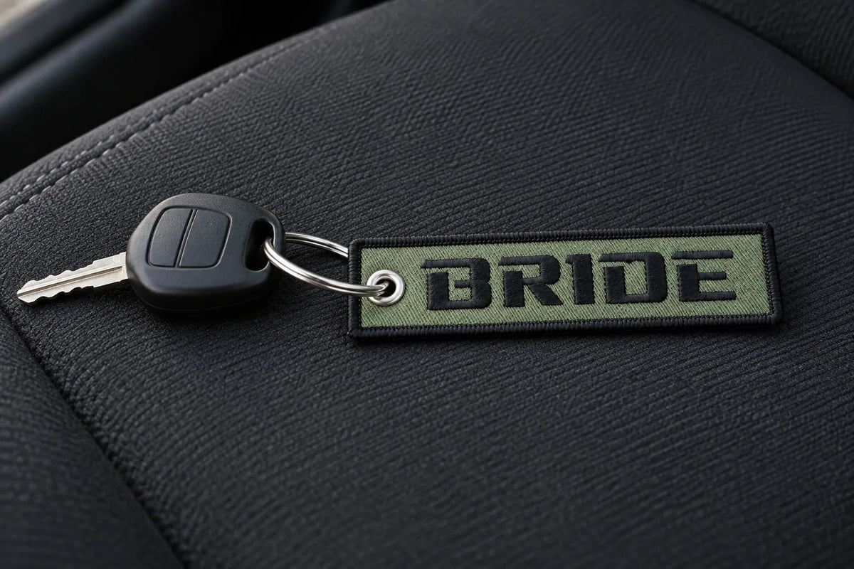 BRIDE Logo Flight Tag Key Chain on a car key resting on a black fabric car seat