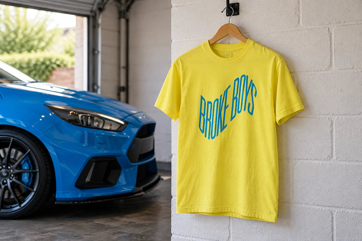 Broke Boys Wave bright yellow tee on a hanger in a garage next to a blue hatchback