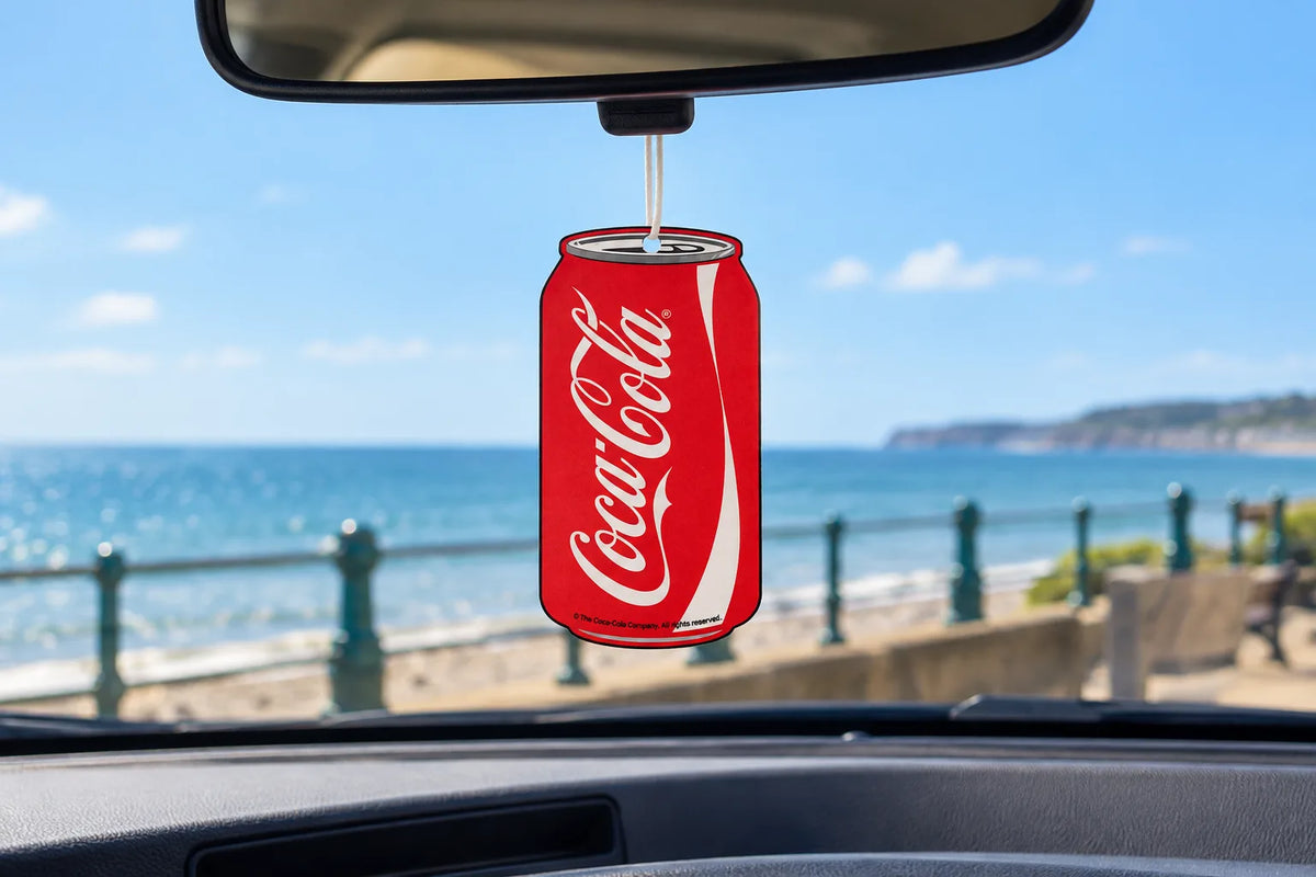 Coca-Cola can car air freshener hanging from a rear-view mirror with the seaside seen through the windscreen