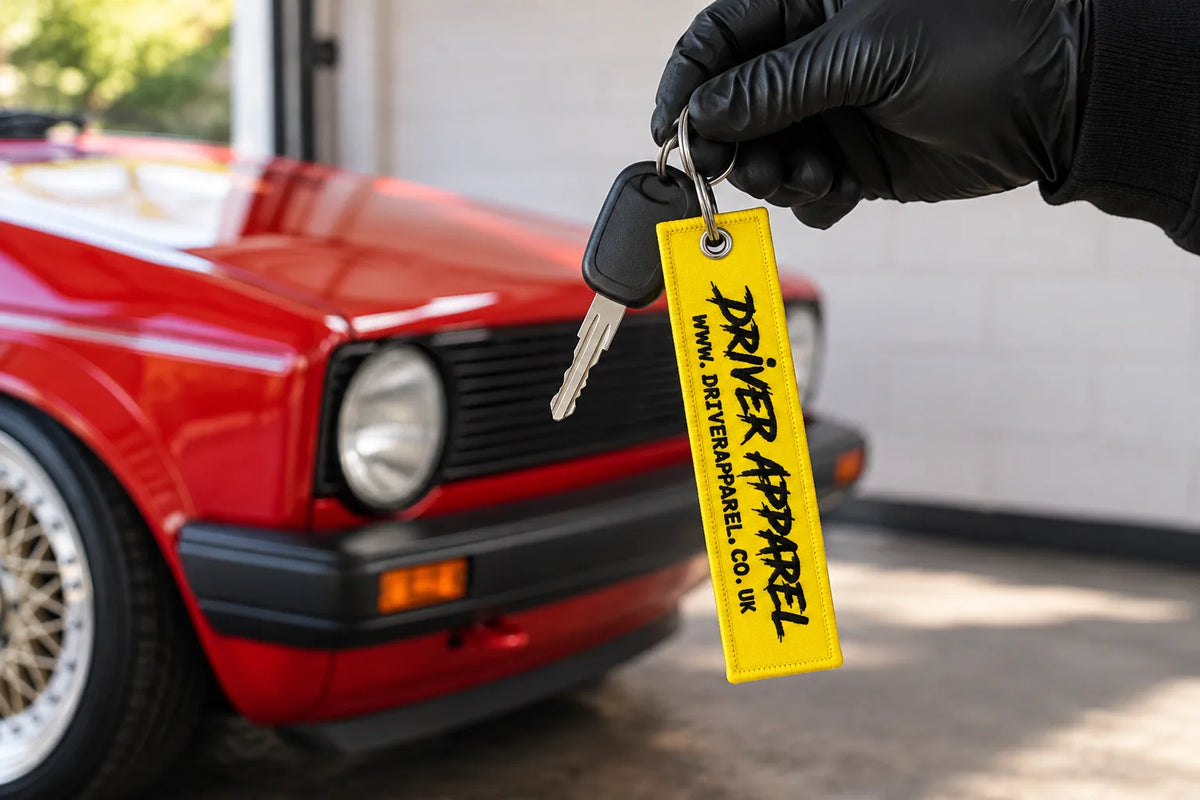 Driver Apparel yellow flight tag key chain on a car key in front of a red classic hatchback