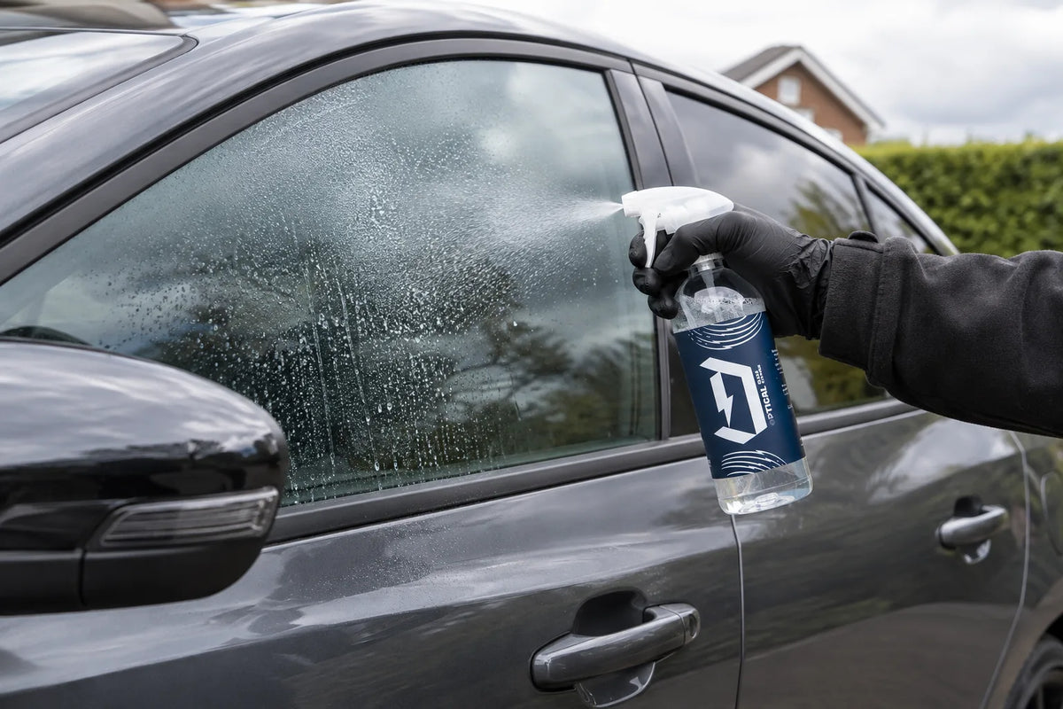 Duel Optical Window & Glass Cleaner being sprayed onto the side window of a grey car
