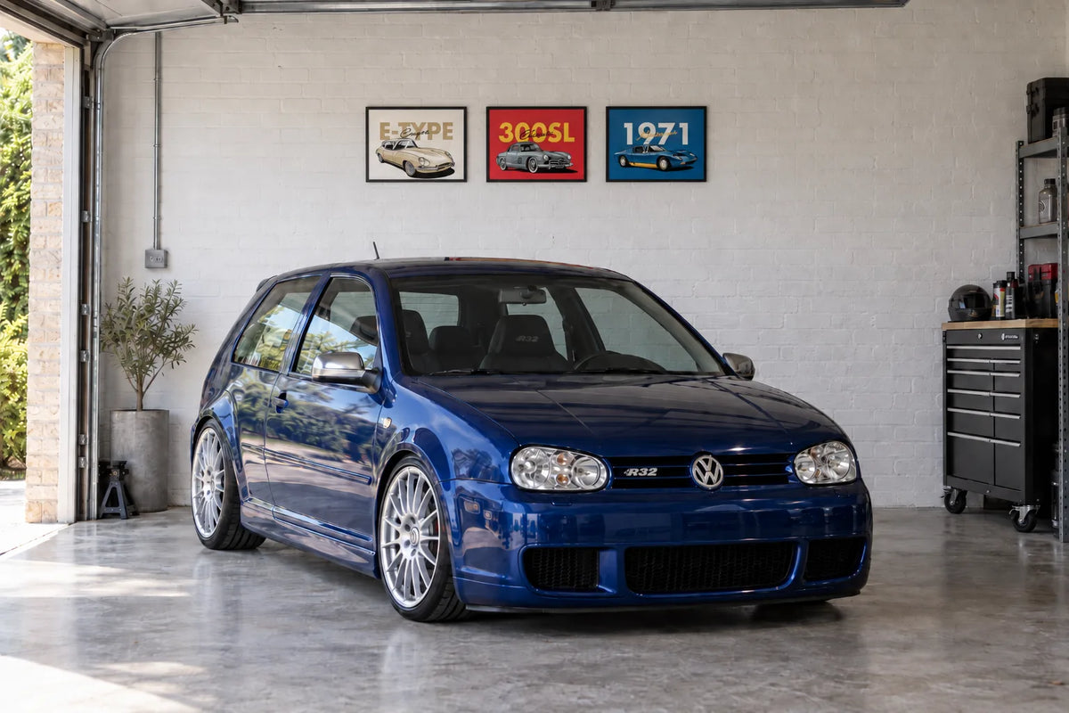 EuroStance E-Type, 300SL and Miura 1971 A3 art posters framed on a garage wall above a blue Volkswagen Golf R32