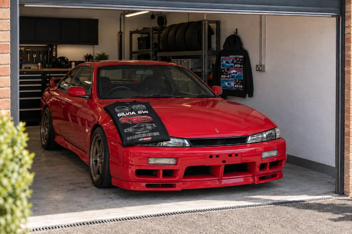 Late Brake Supply Silvia S14 T-shirt on a red Nissan Silvia S14 with the Impreza hoodie on the garage wall