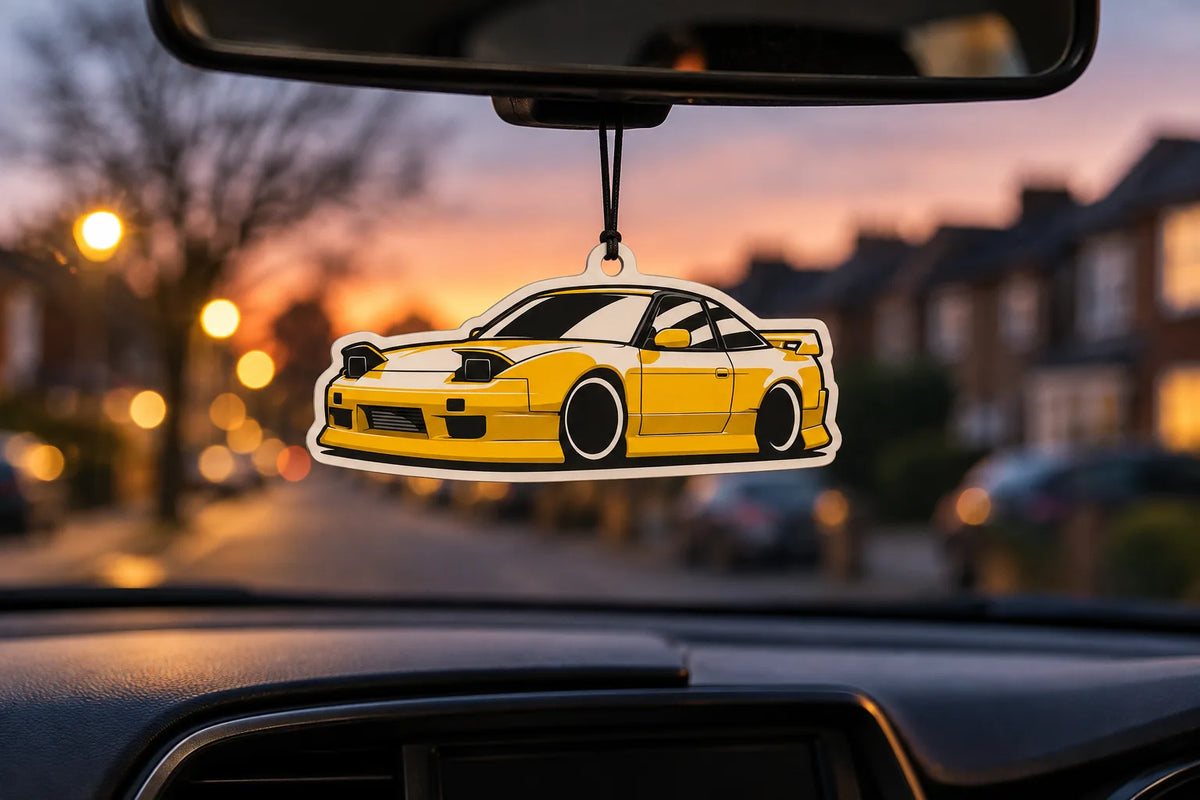 SD Fresh Scents Nissan S13 air freshener hanging from a rear-view mirror at sunset