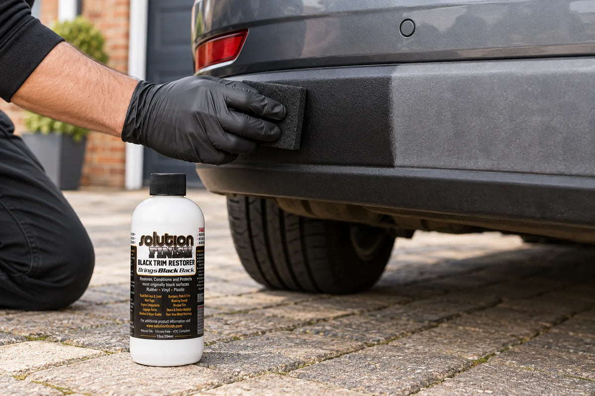 Solution Finish Black Trim Restorer being wiped onto a car's plastic bumper trim, the 12oz bottle on the driveway