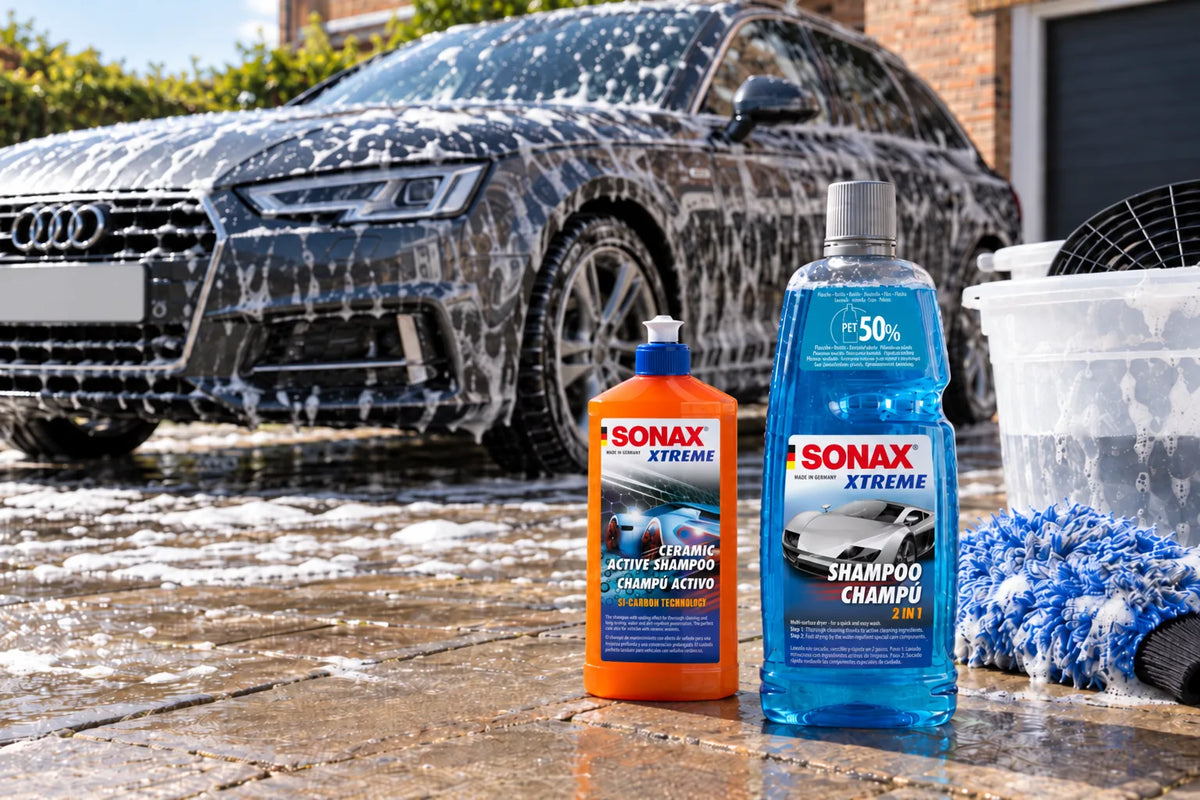 Sonax XTREME Ceramic Active Shampoo and Sonax XTREME Shampoo 2 in 1 on a wet driveway beside a wash bucket while a grey Audi A4 Avant is hand washed