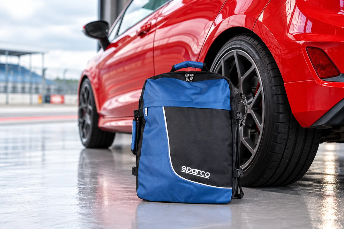 Sparco large blue backpack on a pit lane floor beside the rear wheel of a red hatchback
