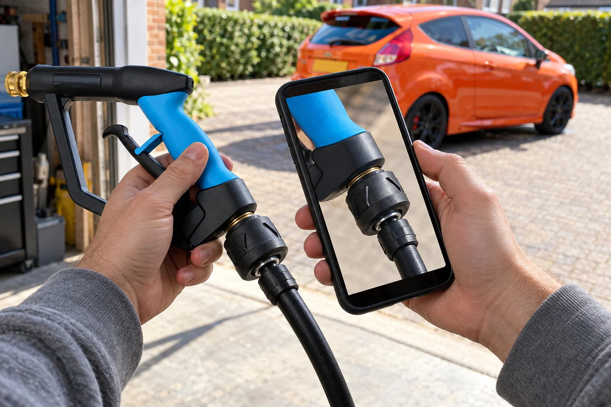 Hand holding a phone to photograph a Better Detailing Karcher Stubby Trigger Gun Adapter fitted between a pressure washer hose and a DTLR reverse short trigger gun, orange hatchback on the driveway behind