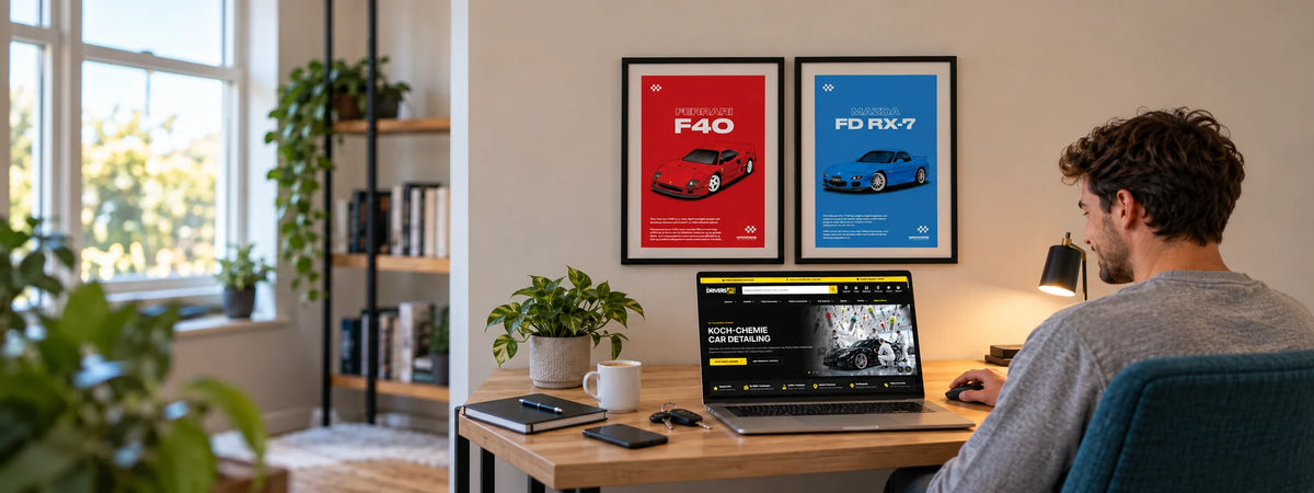 Car enthusiast at a home office desk browsing The Drivers HQ website on a laptop, with Grid Icons Ferrari F40 and Mazda RX-7 car art prints on the wall