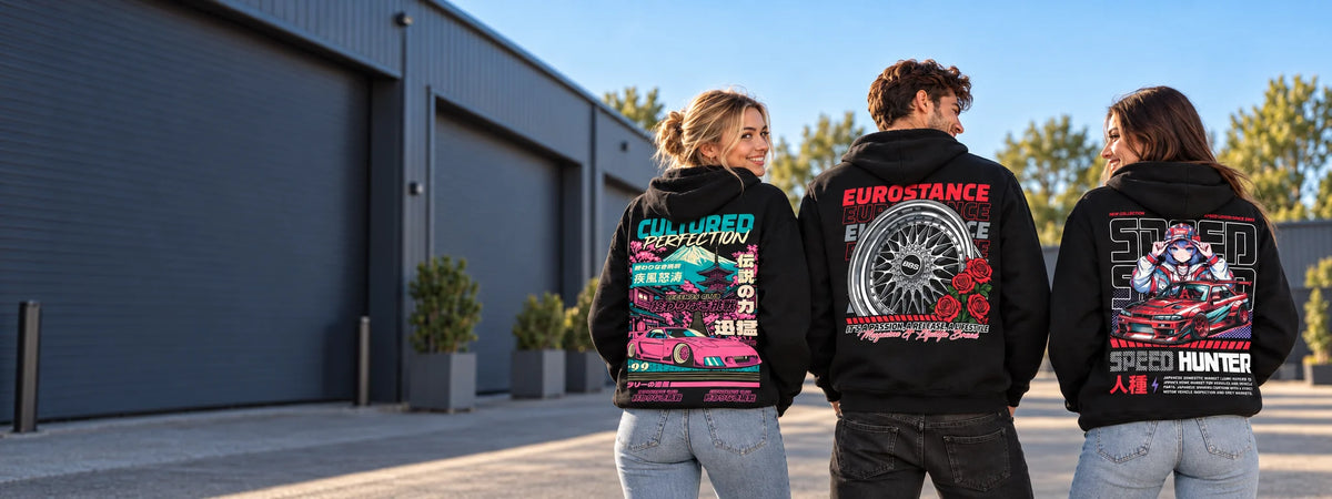 Three friends wearing the EuroStance Legends Club Cultured RX-7, BBS & Roses and Speed Hunter Dope hoodies, back prints to the camera, outside a car workshop on a sunny evening