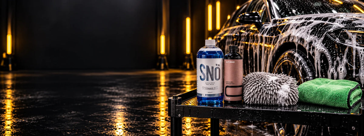 Safe wash kit on a trolley: Stjärnagloss SNÖ snow foam, AutoBead Ceramic Shampoo, a FibreKing Gold Label wash mitt and a Silver Label drying towel by a foamed car