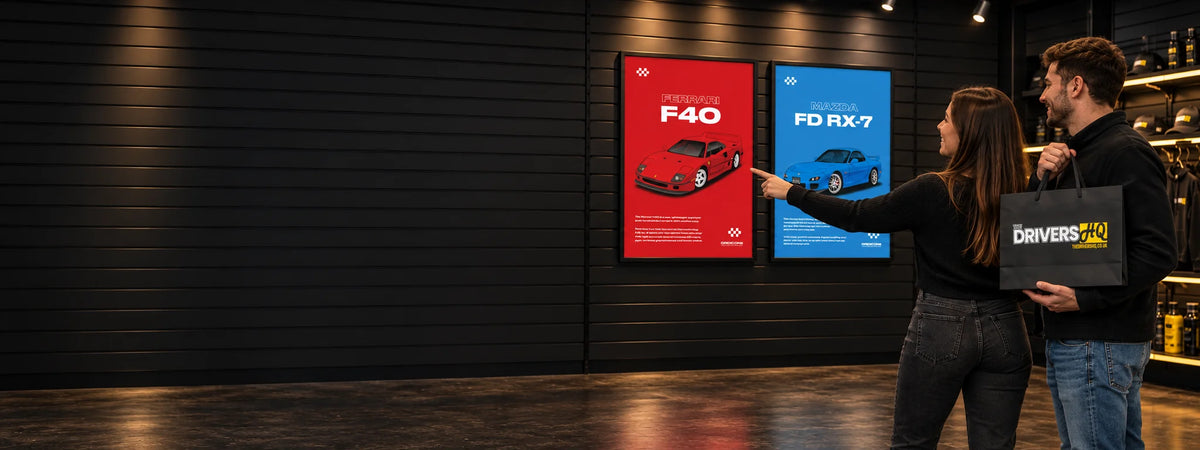 Couple in The Drivers HQ store looking at framed Grid Icons Ferrari F40 and Mazda FD RX-7 posters, holding a The Drivers HQ shopping bag