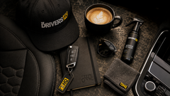 Cap, car key, notebook, sunglasses, coffee cup, spray bottle and microfibre cloth beside a car seat.