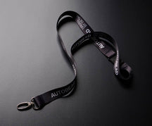 Autobead black lanyard printed AUTOBEAD and DRIVEN BY DETAIL with a metal clip on a dark grey background